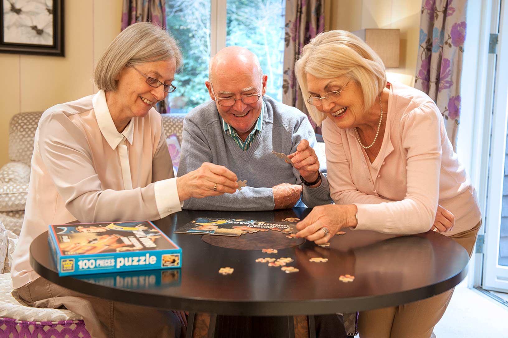 Three residence sitting around a table, focused on a jigsaw puzzle, enjoying the moment together.