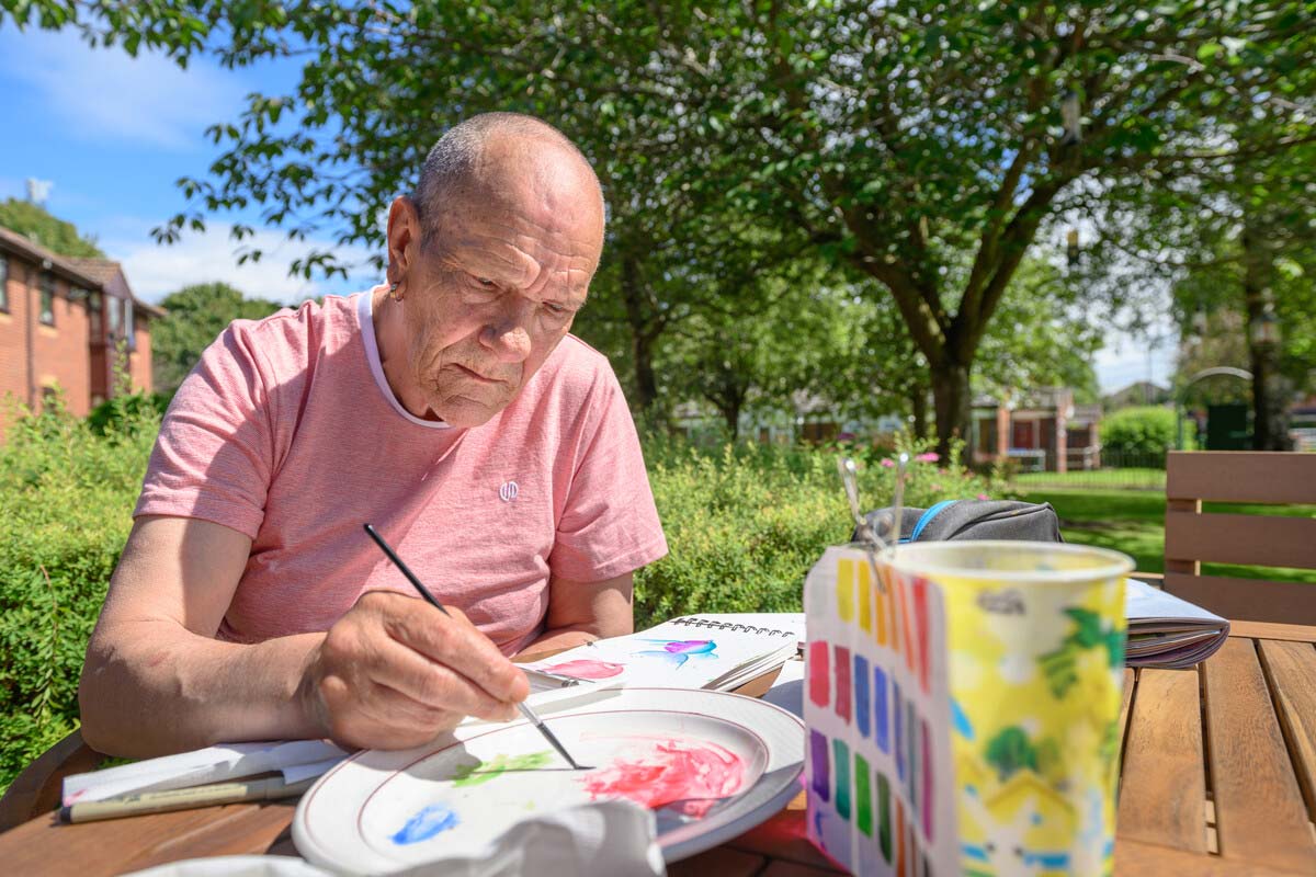 An artist passionately paints on an outdoor table in the communal area of Anchor, creating art pieces with vibrant colours.