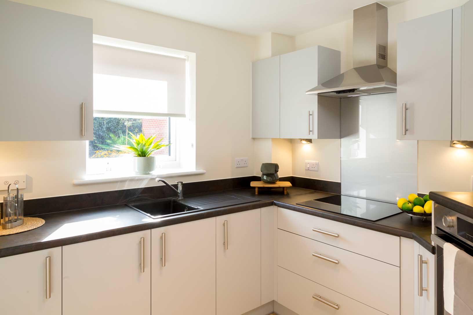 A modern kitchen with white storage cupboards, a window with a garden view and electric stove for safety.