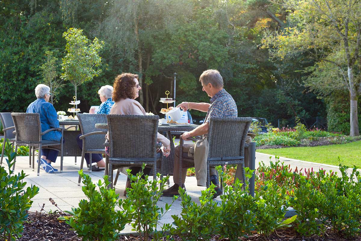 An idyllic garden setting where people relax and socialise at outdoor tables, amidst blooming flowers and greenery.